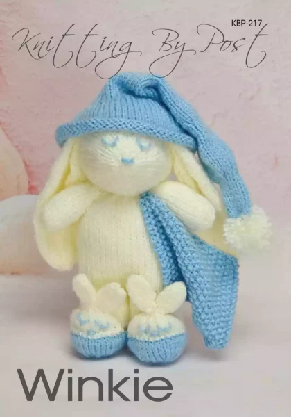 Winkie the Bunny knitting pattern. Cream-colored knitted toy rabbit approximately 23cm tall, featuring a blue sleeping cap, matching blanket, and removable slippers.