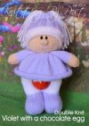 Violet with a Chocolate Egg knitting pattern. Easter-themed knitted toy doll approximately 25cm tall, featuring a lilac dress and white bonnet, with space under her skirt to hold a small chocolate egg.