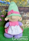 Gnorma the Gnome knitting pattern. Cream-colored knitted toy gnome approximately 30cm tall, featuring a lilac dress, pink apron, and light green hat, embodying a whimsical garden theme.