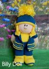 Billy Dolly knitting pattern. Cream-colored knitted toy doll approximately 35cm tall, featuring a blue outfit with yellow accents and a pom-pom hat, embodying a playful theme.