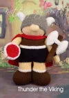 Thunder the Viking knitting pattern. Norse-themed knitted toy approximately 30cm tall, featuring a removable helmet, cape, axe, jumper, and shield.