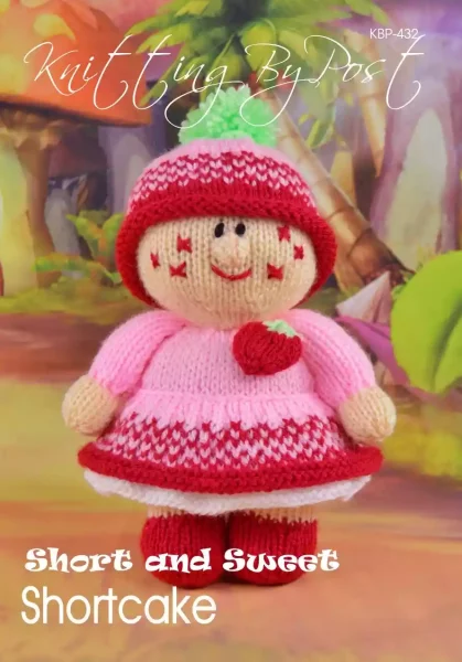 Short and Sweet Shortcake knitting pattern. Cream-colored knitted toy doll approximately 20cm tall, featuring a pink dress, red accents, and a green hat with a pom-pom, embodying a strawberry theme.