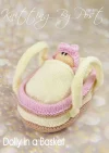 Dolly in a Basket knitting pattern play set – cream-colored knitted basket measuring approximately 18cm long and 11cm wide, containing a 12cm tall pink knitted doll, both crafted with double knitting yarn