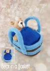 Bear in a Basket knitting pattern. Cream-colored knitted toy bear approximately 12cm tall, nestled in a light blue basket measuring approximately 18cm long and 11cm wide.