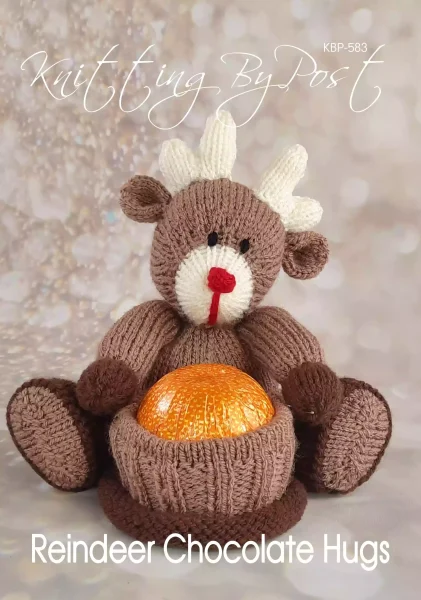 Reindeer Chocolate Hugs knitting pattern. Christmas-themed knitted toy reindeer approximately 18cm tall when seated, designed to hold a chocolate orange within its body. Features light brown and dark brown yarn, with red and cream accents.