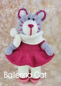 A knitted plush cat toy made from a knitting pattern, featuring a gray and white body, pink embroidered facial details, and black stitched eyes. The cat is dressed in a red knitted skirt, a white scarf, and matching pink shoes. It stands upright against a sparkling, soft-focus background